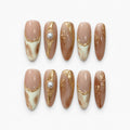 catalog: Long almond press-on nails in warm nude with cream and caramel marbling, raised gold foil lines, and a single cream pearl accent.