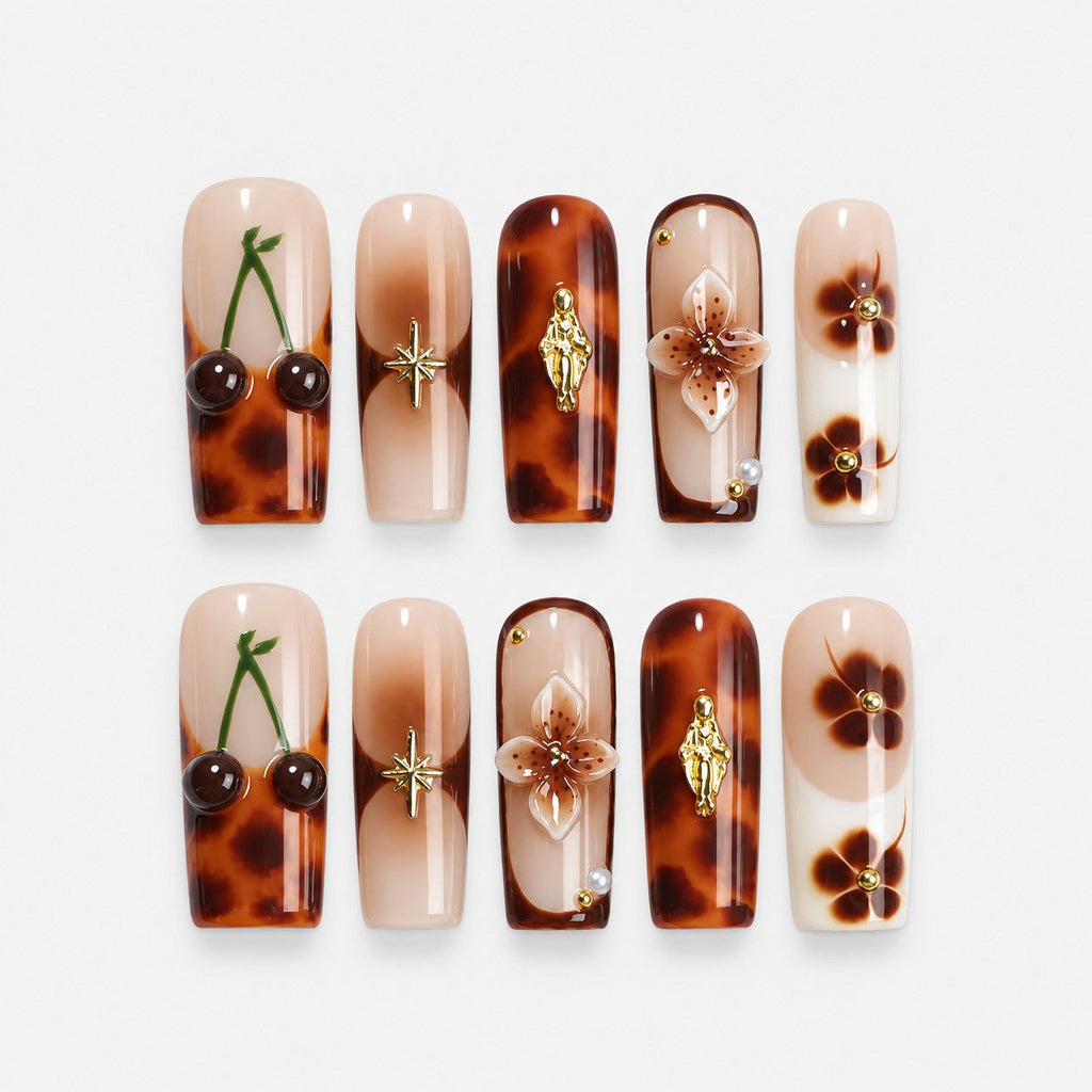 catalog: Long square press-on nails in caramel and brown tortoiseshell with gold flower charms and painted cherries on a nude nail.