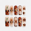 catalog: Long square press-on nails in caramel and brown tortoiseshell with gold flower charms and painted cherries on a nude nail.