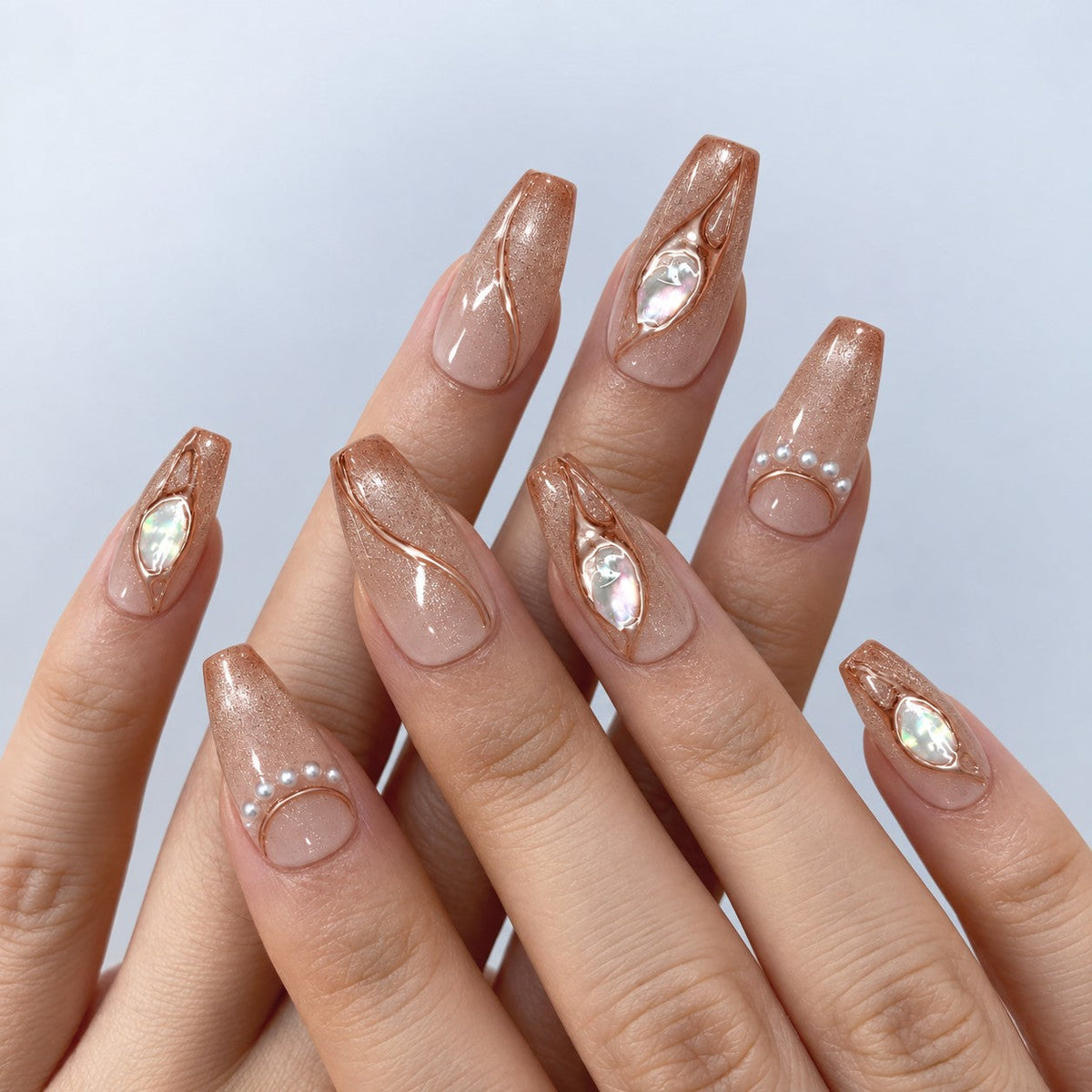 hand: Medium coffin press-on nails in warm nude with bronze cat-eye shimmer, raised clear swirls, opal stones and a row of small pearls.
