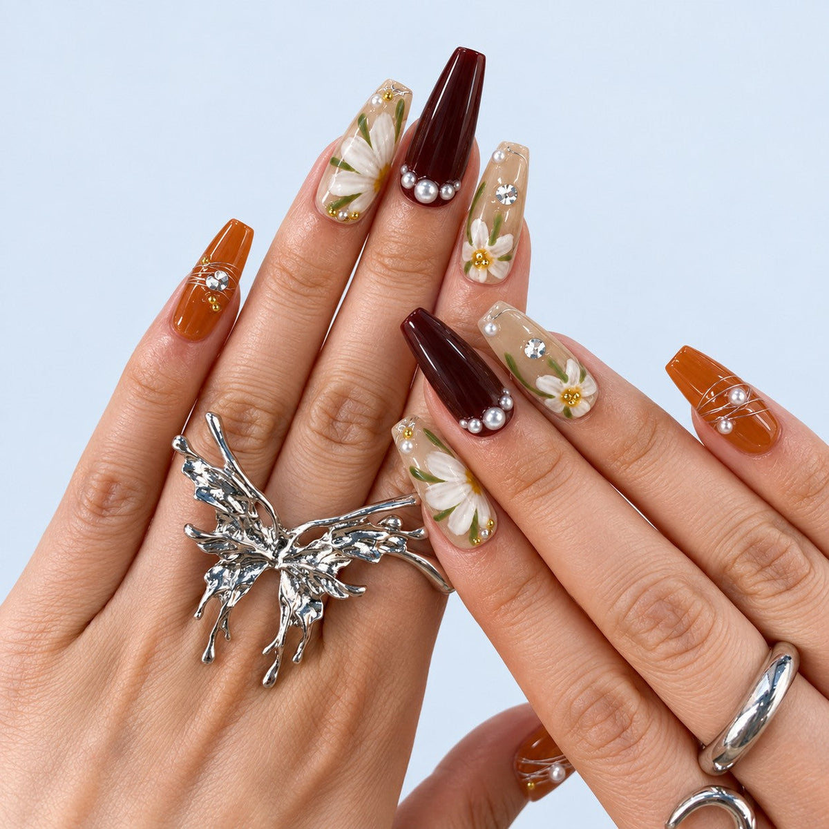 hand: Long coffin press-on nails in amber, dark wine and sheer honey, with hand-painted white daisies, gold wire wrapping, pearls and crystals.