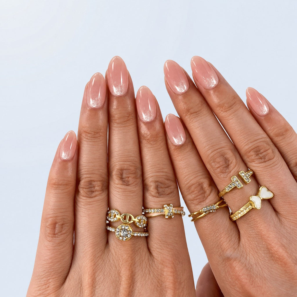 hand: Short almond nails in sheer pink nude with glossy finish and shimmering pale champagne French tips.