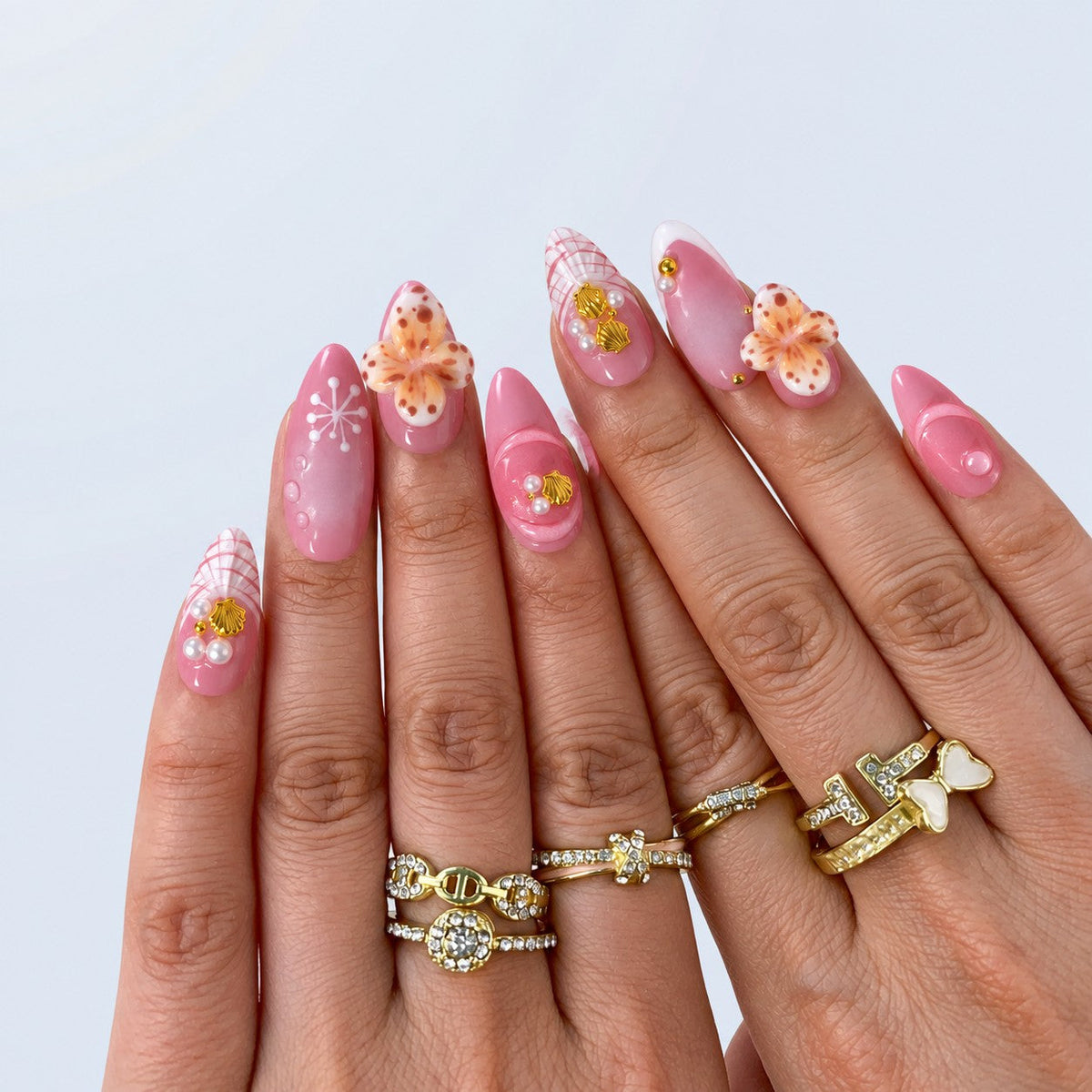 hand: Almond medium press-on nails in rose pink with white tips, sculpted cream and apricot flowers, gold shell charms and pearls.