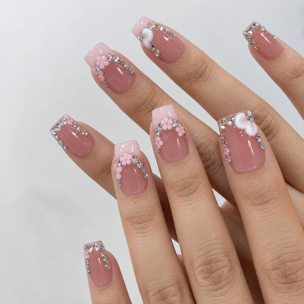 hand: Medium square press-on nails in dusty rose with a milky pink French tip, rhinestone clusters, sculpted pink flowers and white hearts.