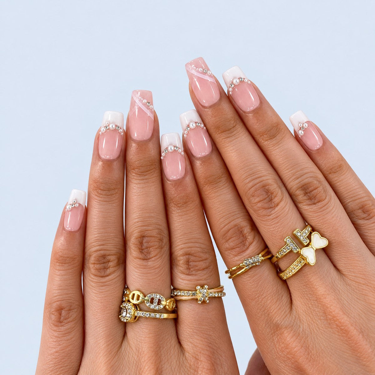 hand: Medium square press-on nails in sheer pink with white French tips, small pearls and clear crystals along the smile line.