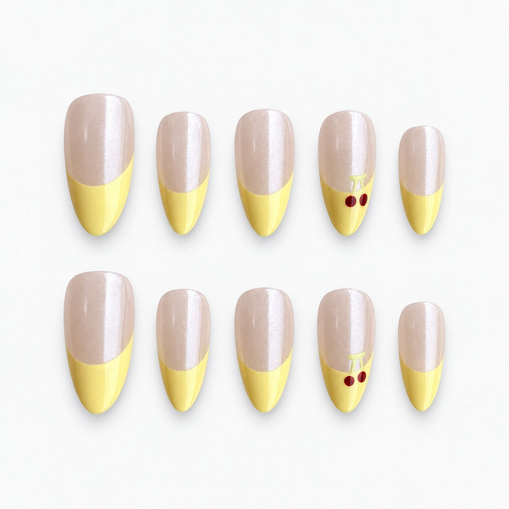 catalog: Medium almond press-on nails with a pearly nude base, pastel yellow French tips and small red painted cherries on one accent nail.