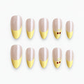 catalog: Medium almond press-on nails with a pearly nude base, pastel yellow French tips and small red painted cherries on one accent nail.