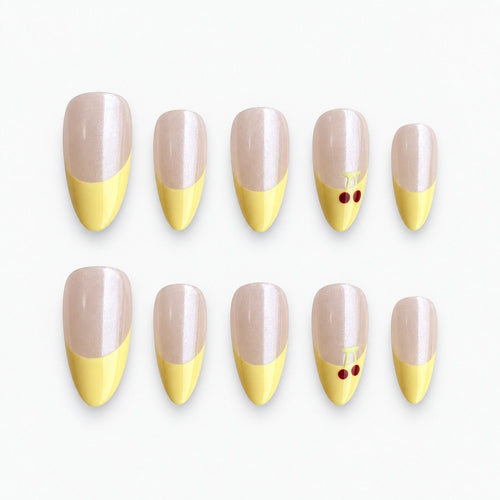 catalog: Medium almond press-on nails with a pearly nude base, pastel yellow French tips and small red painted cherries on one accent nail.