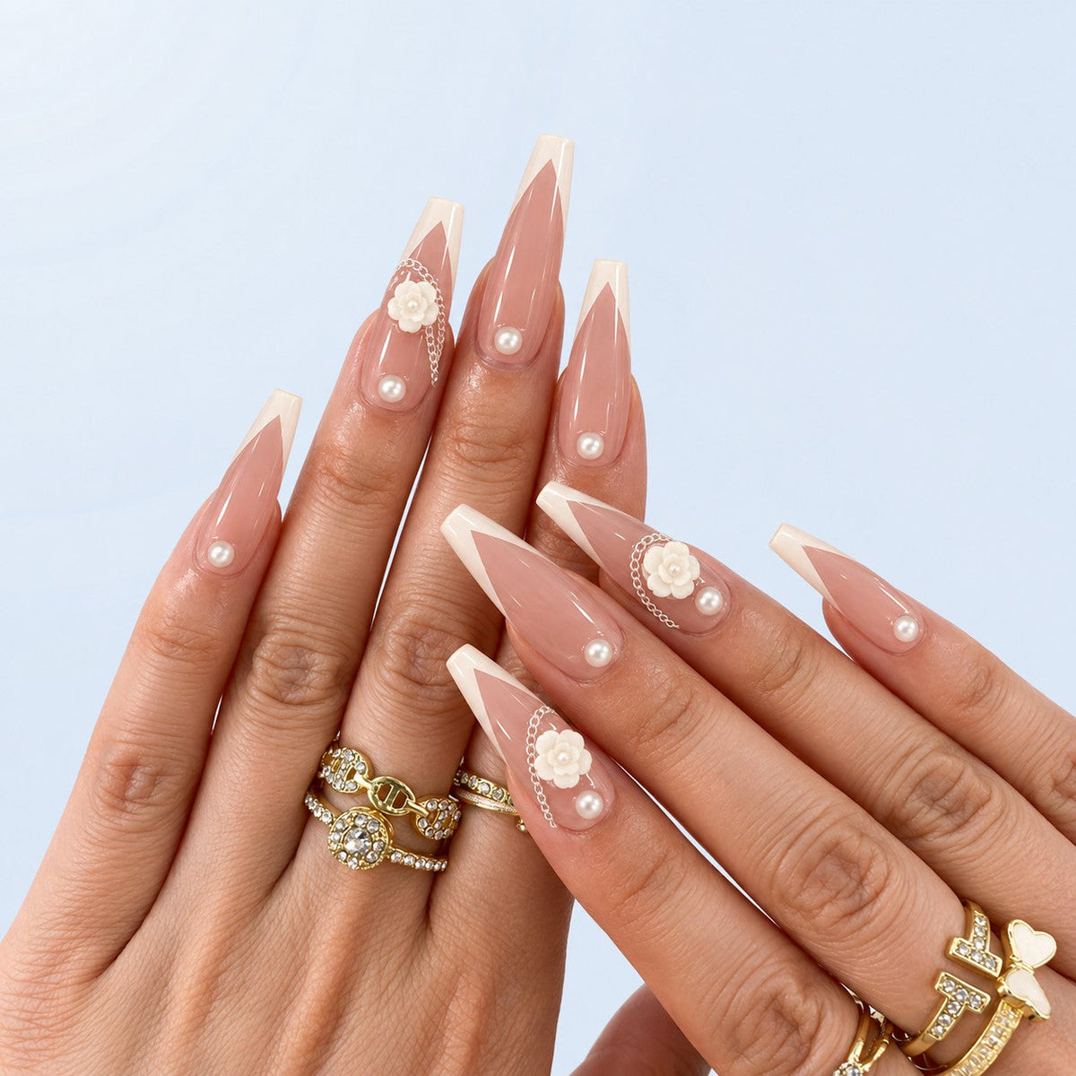 hand: Long almond press-on nails with sheer blush base, soft white French tips, a sculpted white camellia flower, a silver chain and single pearls.