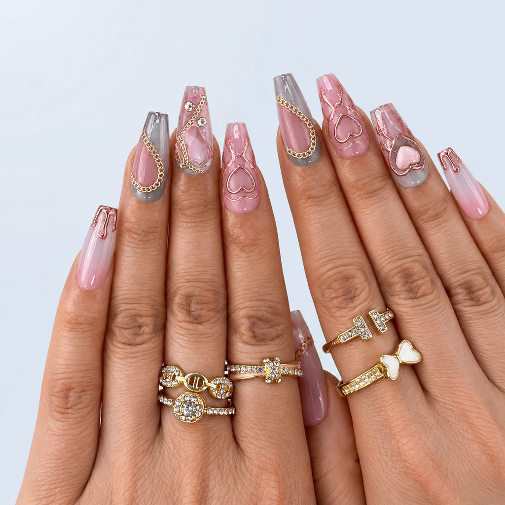 hand: Long coffin press-on nails in smoky grey and dusty rose with silver chains, raised pink hearts and clear crystals.