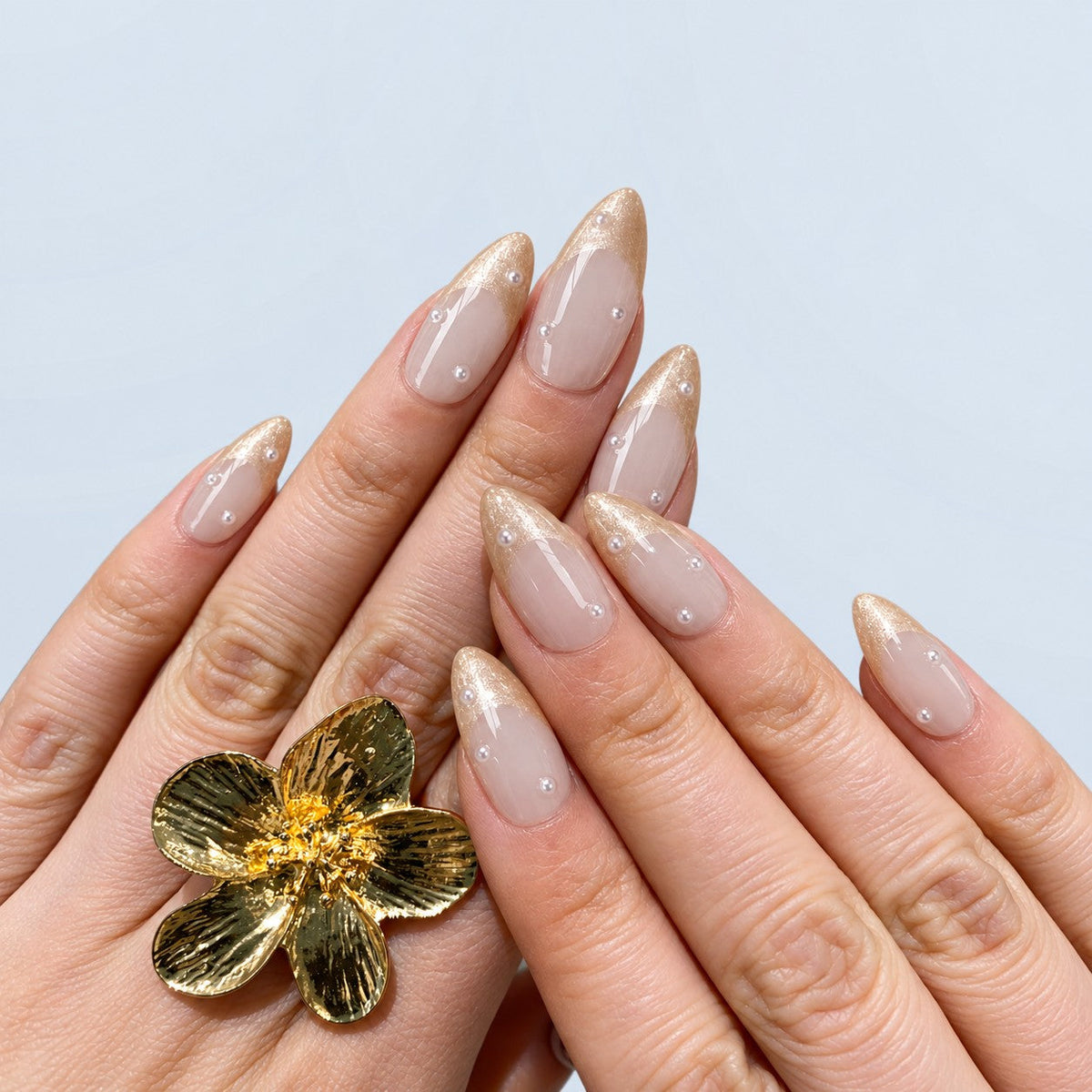 hand: Medium almond press-on nails with a milky blush base, shimmering champagne French tips and small scattered pearls.