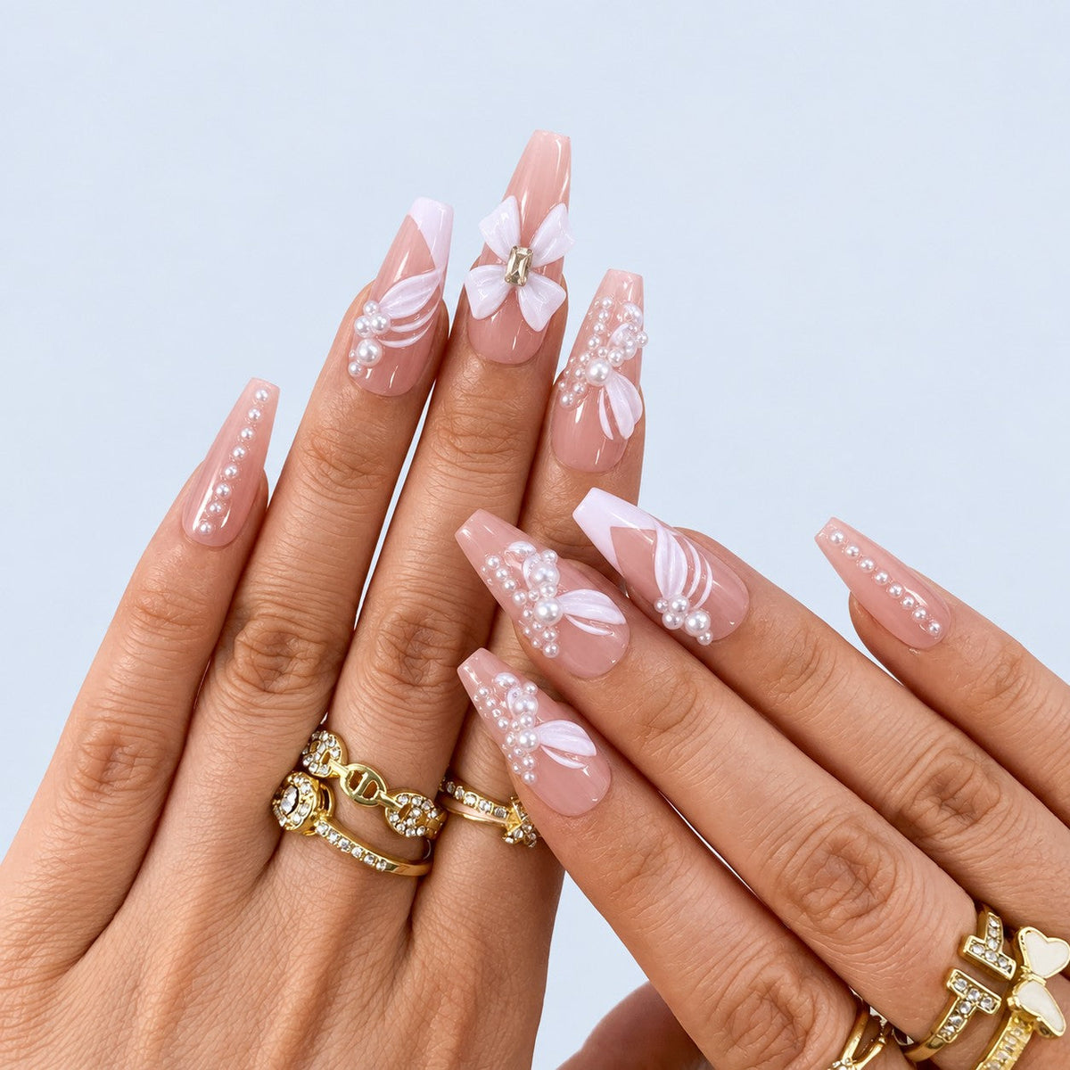 hand: Long nude coffin nails with white French tips, a large white sculpted bow and rows of small pearls.