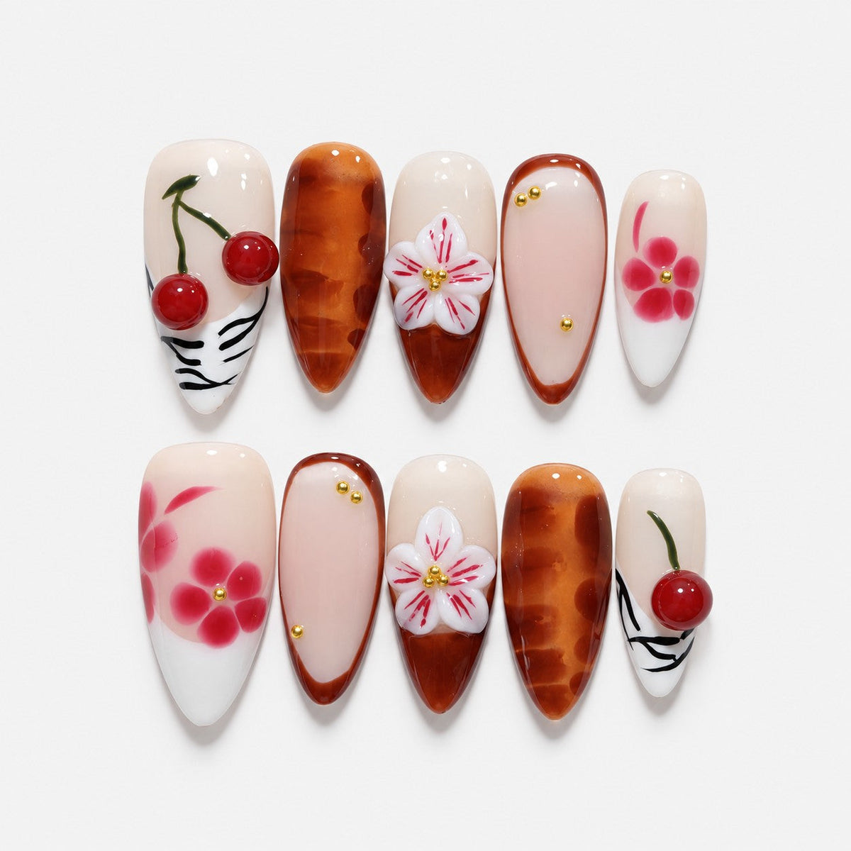 catalog: Long almond press-on nails in cream and amber brown with 3D red cherries, sculpted white lilies and painted pink blossoms.