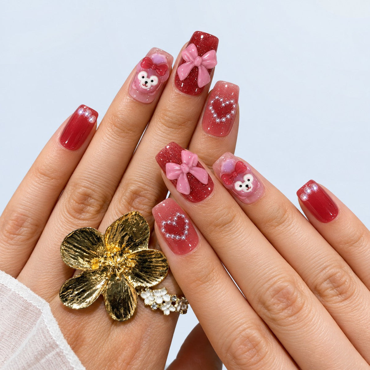hand: Medium square press-on nails in cherry red and mauve with a pink 3D bow, a bear charm and small pearl accents.