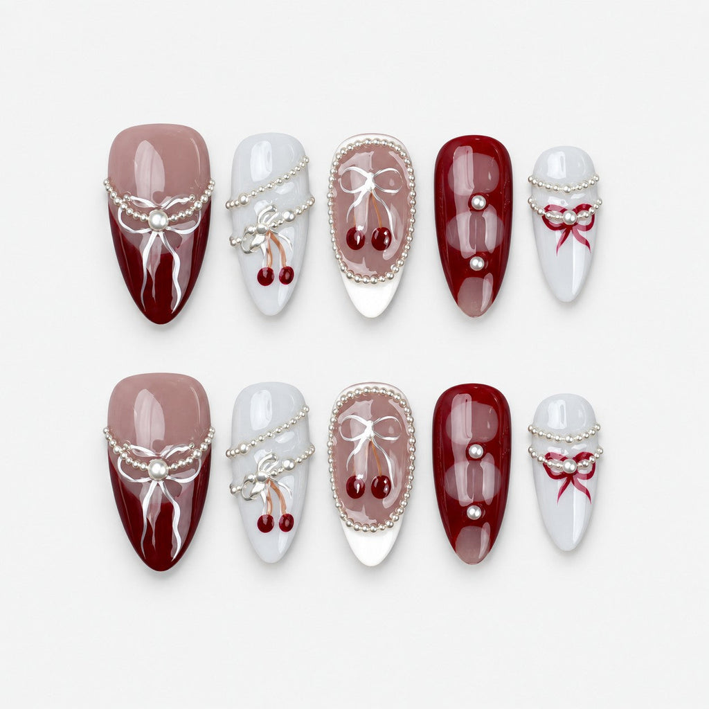 catalog: Medium almond press-on nails in burgundy, mauve and grey with painted white bows, silver bead strands and glossy red cherry charms.
