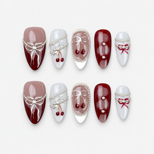 catalog: Medium almond press-on nails in burgundy, mauve and grey with painted white bows, silver bead strands and glossy red cherry charms.