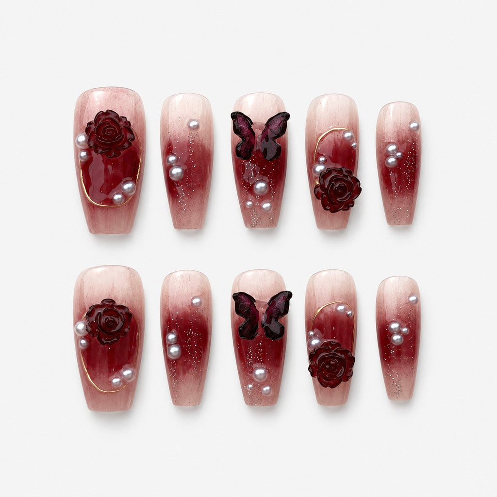 catalog: Coffin shaped press-on nails with a wine red to nude gradient, sculpted dark red roses, a carved butterfly, grey pearls and fine gold lines.