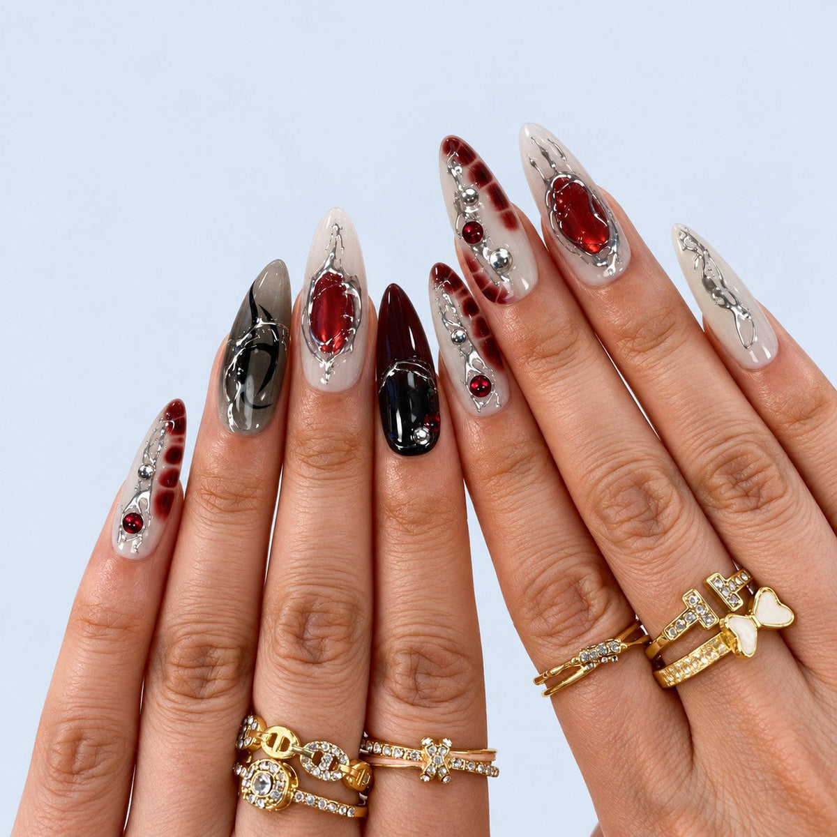 hand: Long almond press-on nails in smoky grey and black with red stones, silver chrome veins and a sculpted spider.