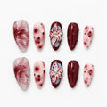 catalog: Medium almond press-on nails in wine red and blush pink with a sculpted three dimensional lily flower, marbled swirls and raised glossy dots.