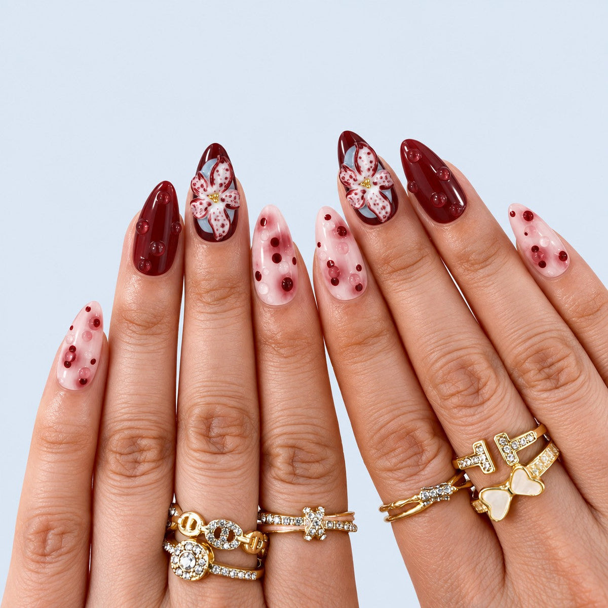 hand: Medium almond press-on nails in wine red and blush pink with a sculpted three dimensional lily flower, marbled swirls and raised glossy dots.