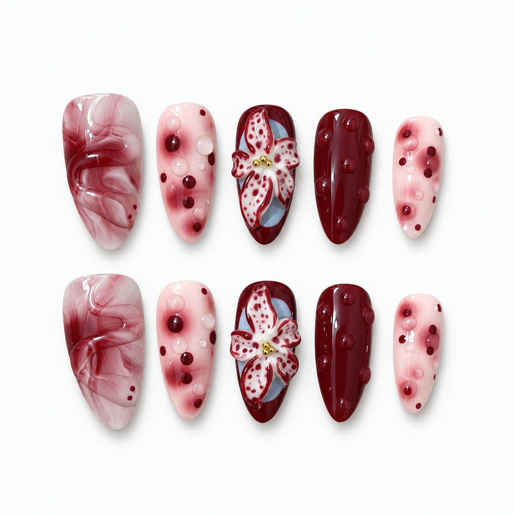catalog: Medium almond press-on nails in wine red and blush pink with marbling, raised glossy dots and a sculpted hand-painted lily.