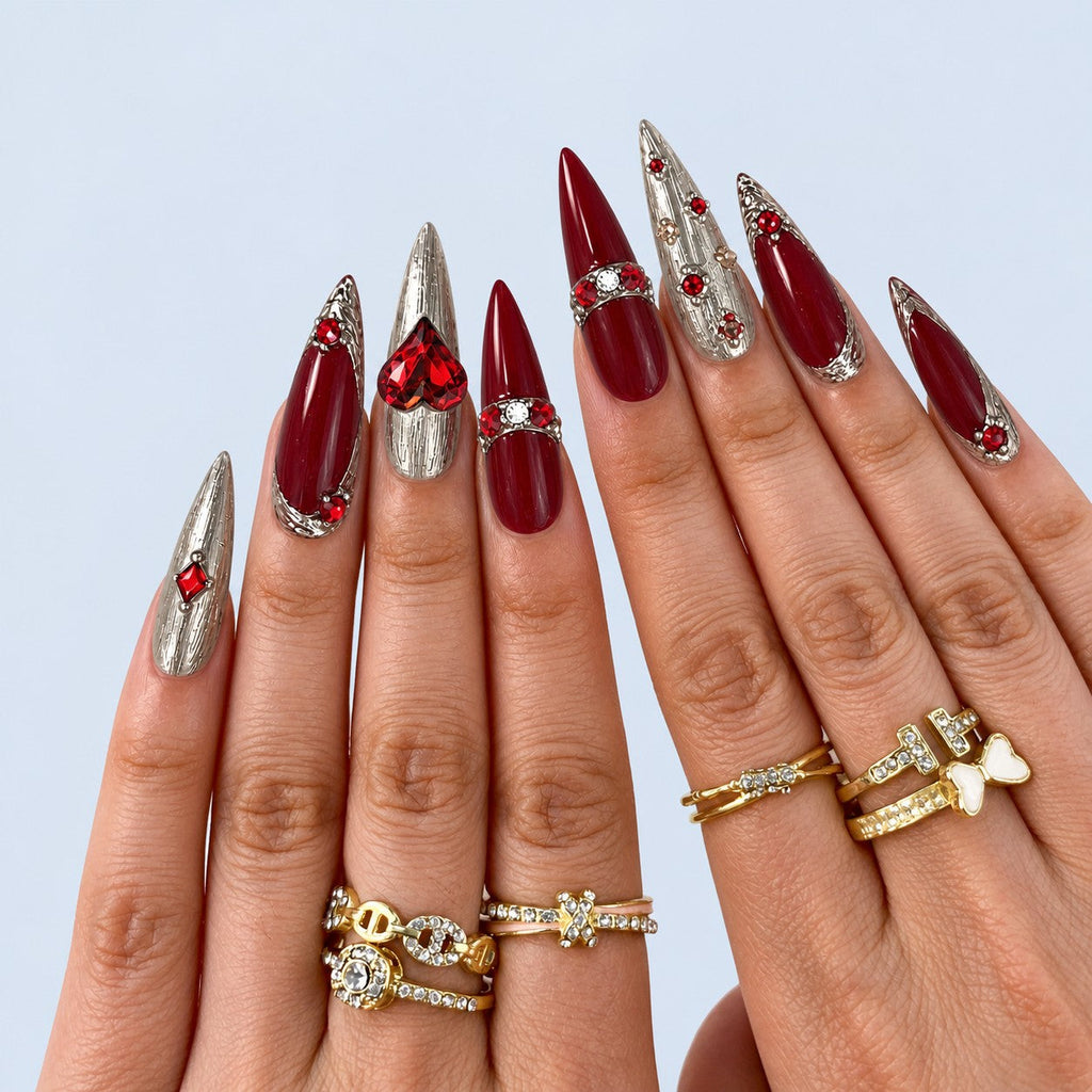 hand: Long stiletto nails in deep red and brushed silver with a faceted red heart stone and scattered red crystals.