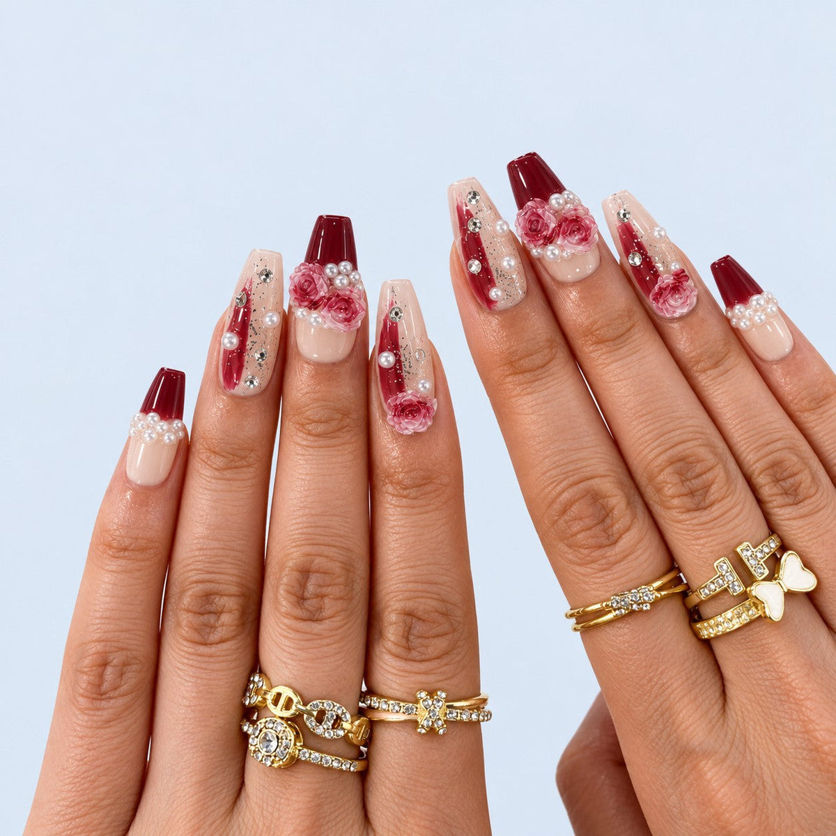 hand: Medium coffin-shaped press-on nails with a dark red to nude gradient, sculpted pink and red roses, white pearls and small crystals.