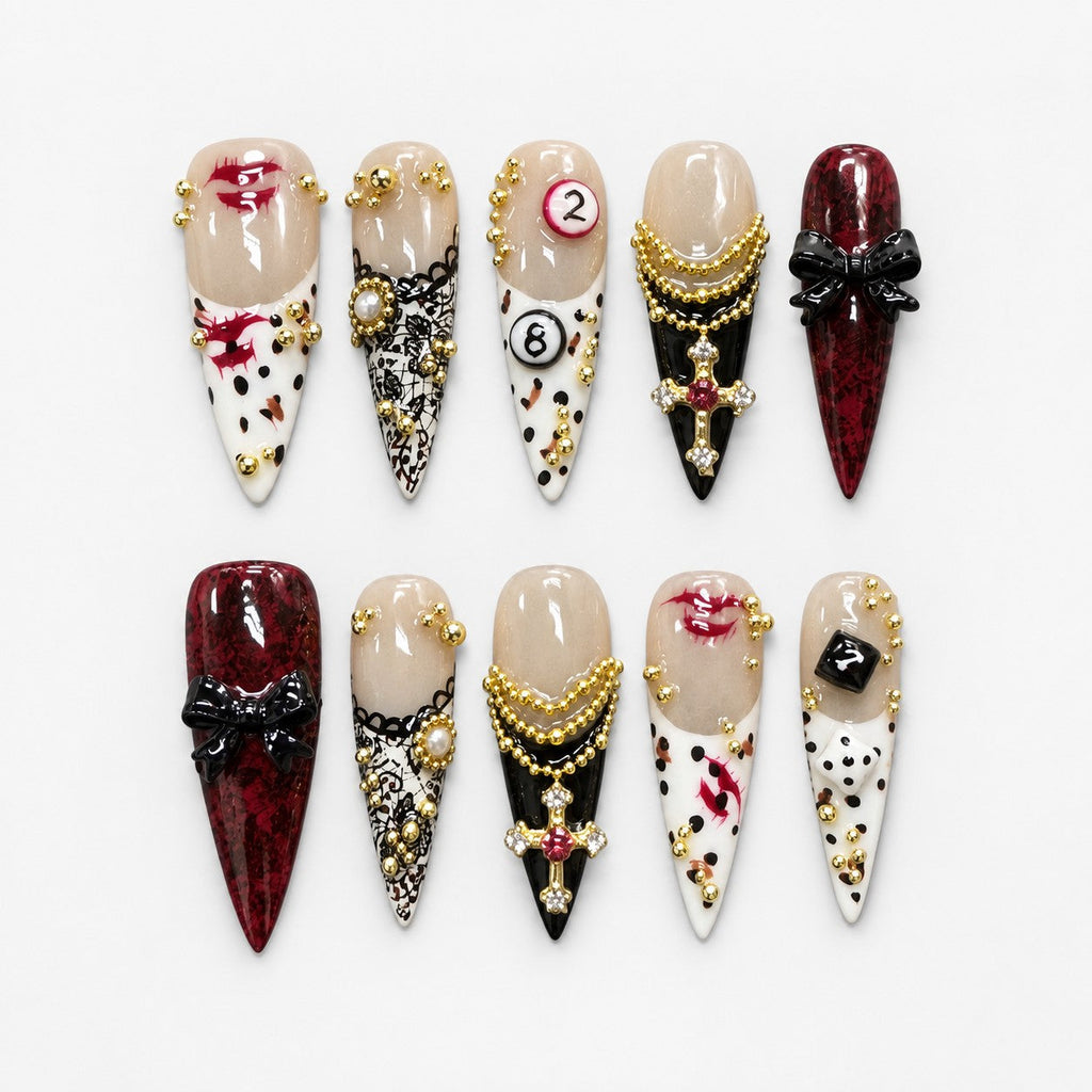 catalog: Long stiletto press-on nails in cream and deep red with gold bead chains, a jewelled cross charm, black bows, lace print and painted red lips.