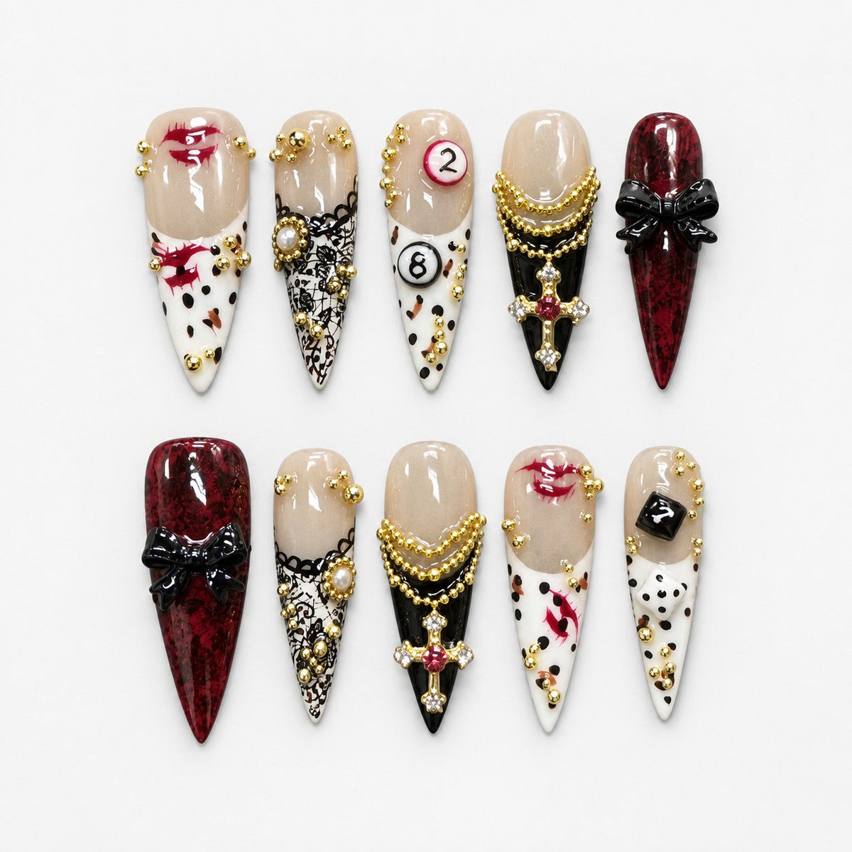catalog: Long stiletto press-on nails in cream and deep red with gold bead chains, a jewelled cross charm, black bows, lace print and painted red lips.