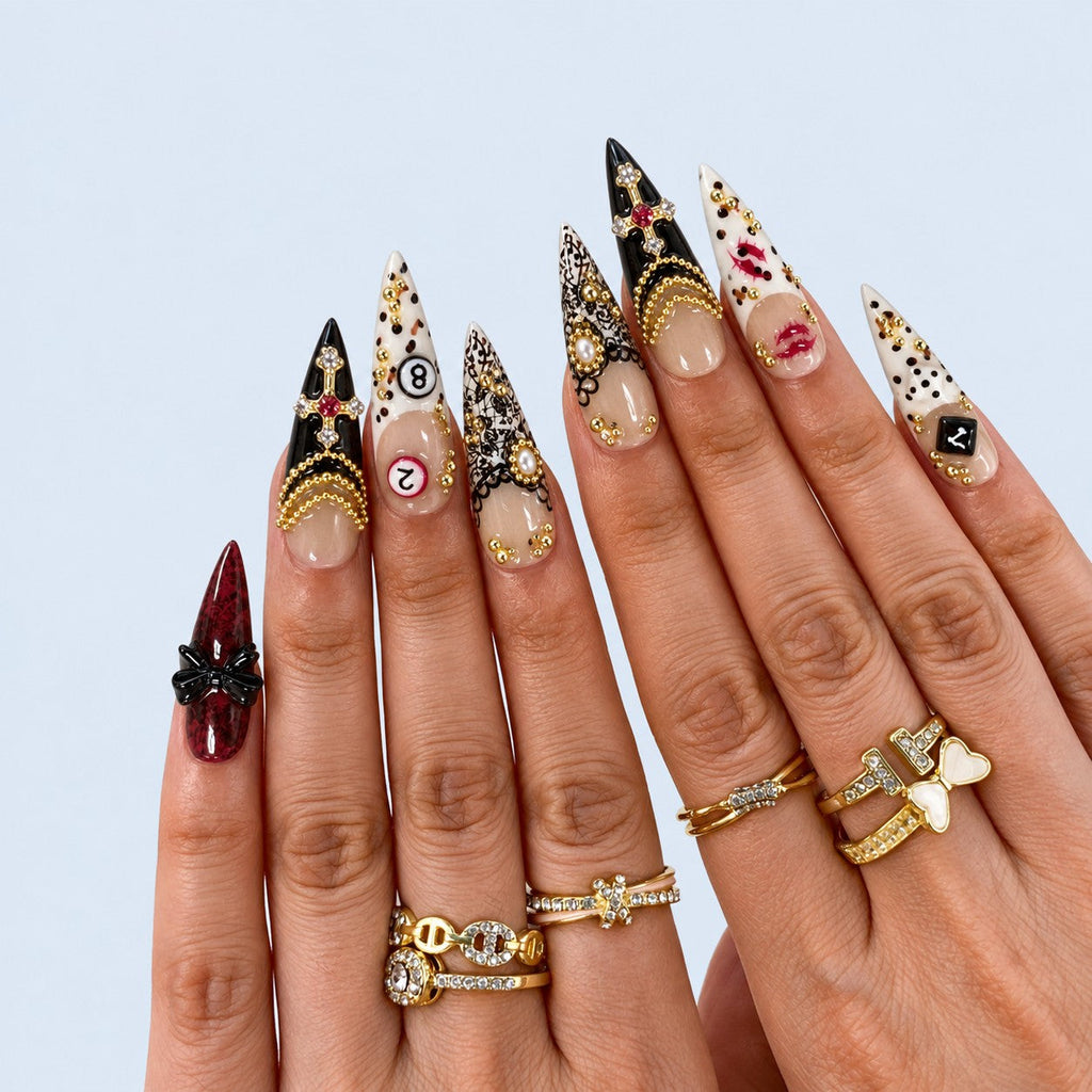 hand: Long stiletto press-on nails in cream and deep red with gold bead chains, a jewelled cross charm, black bows, lace print and painted red lips.