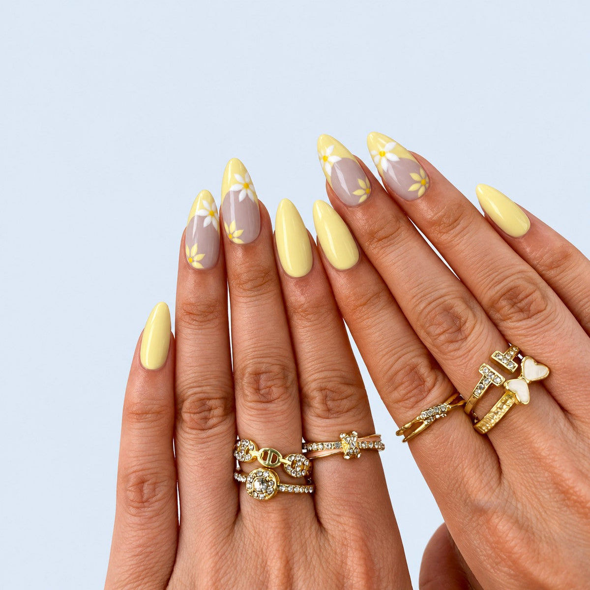 hand: Long almond press-on nails with a pale yellow French tip over a greige base and small hand painted white and yellow daisies.