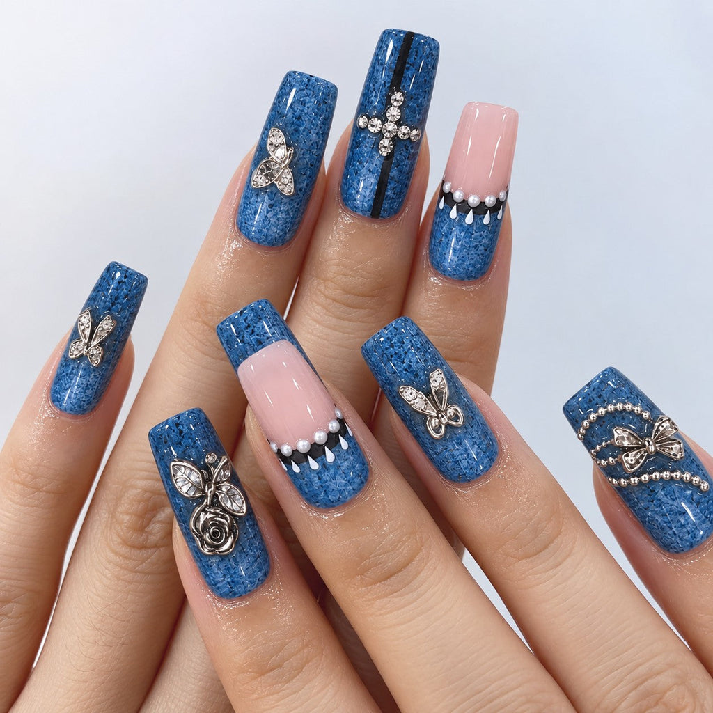 hand: Long square press-on nails in speckled denim blue with sheer pink accents, silver rose and bow charms, pearls and small crystals.