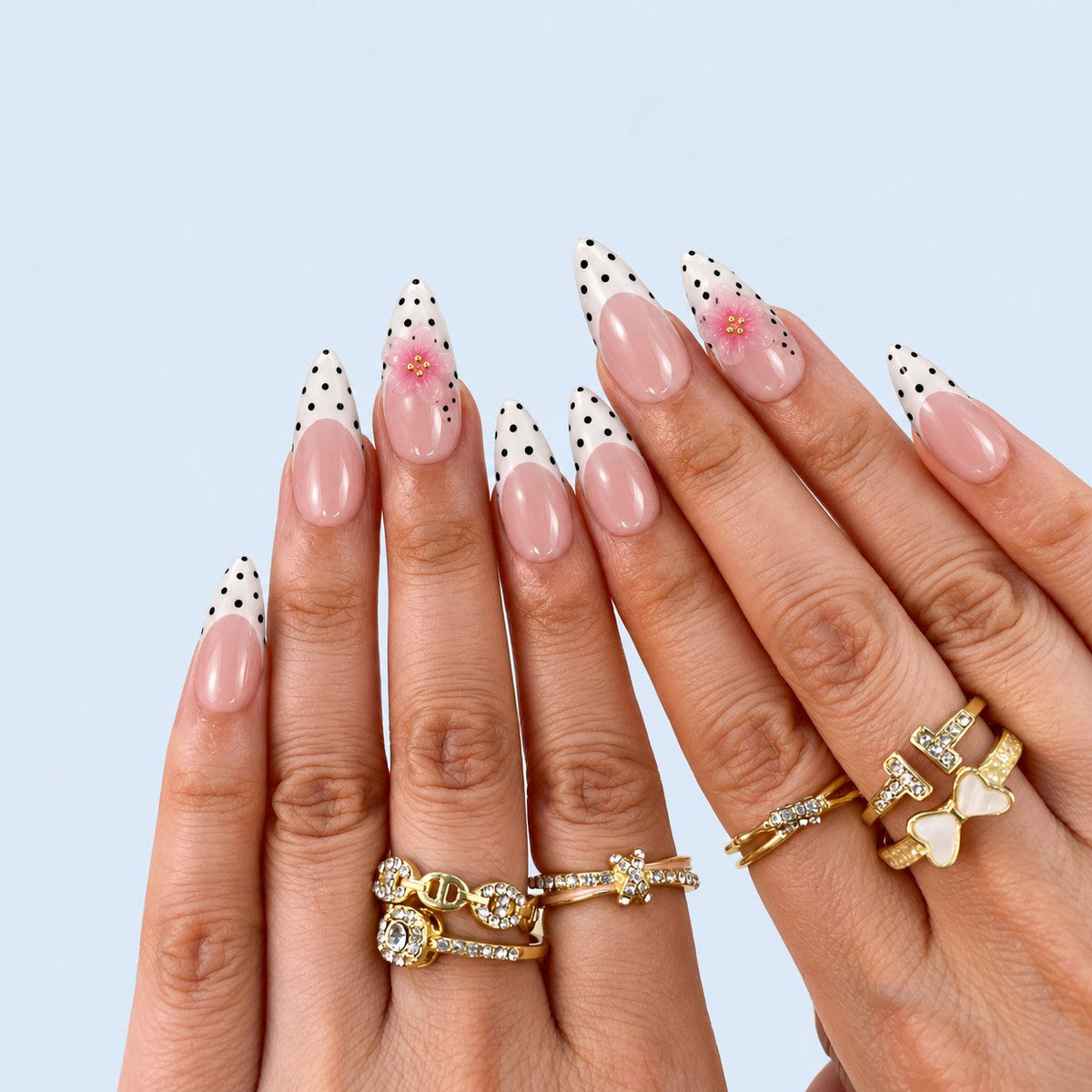 hand: Long almond press-on nails with a sheer pink base, black and white polka dot tips and small sculpted pink flowers with gold centres.