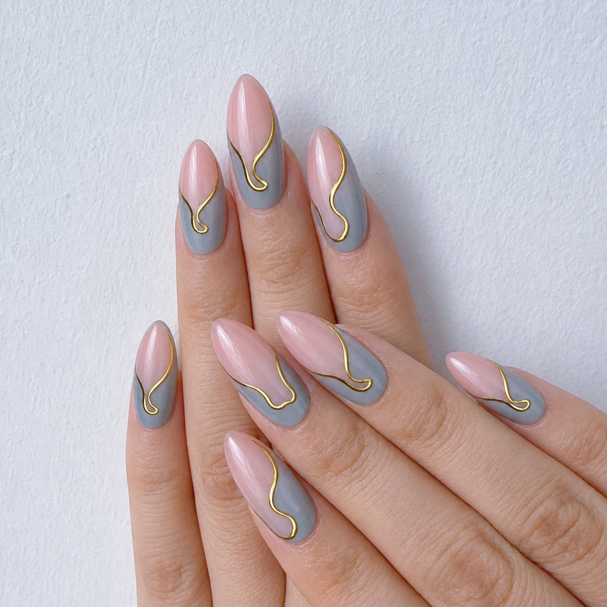 hand: Medium almond press-on nails with a sheer pink base, grey wavy French tips and a thin gold line along each curve.