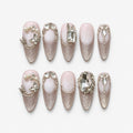 catalog: Long almond press-on nails with milky pink bases, silver cat-eye shimmer, clear faceted crystals, sculpted leaf vines and small pearls.