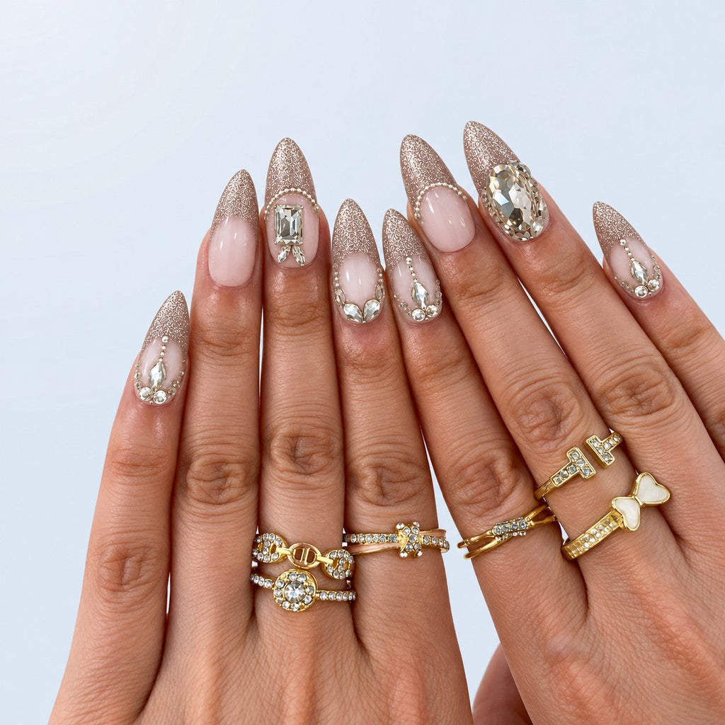 hand: Long almond press-on nails with milky pink bases, silver cat-eye shimmer, clear faceted crystals, sculpted leaf vines and small pearls.