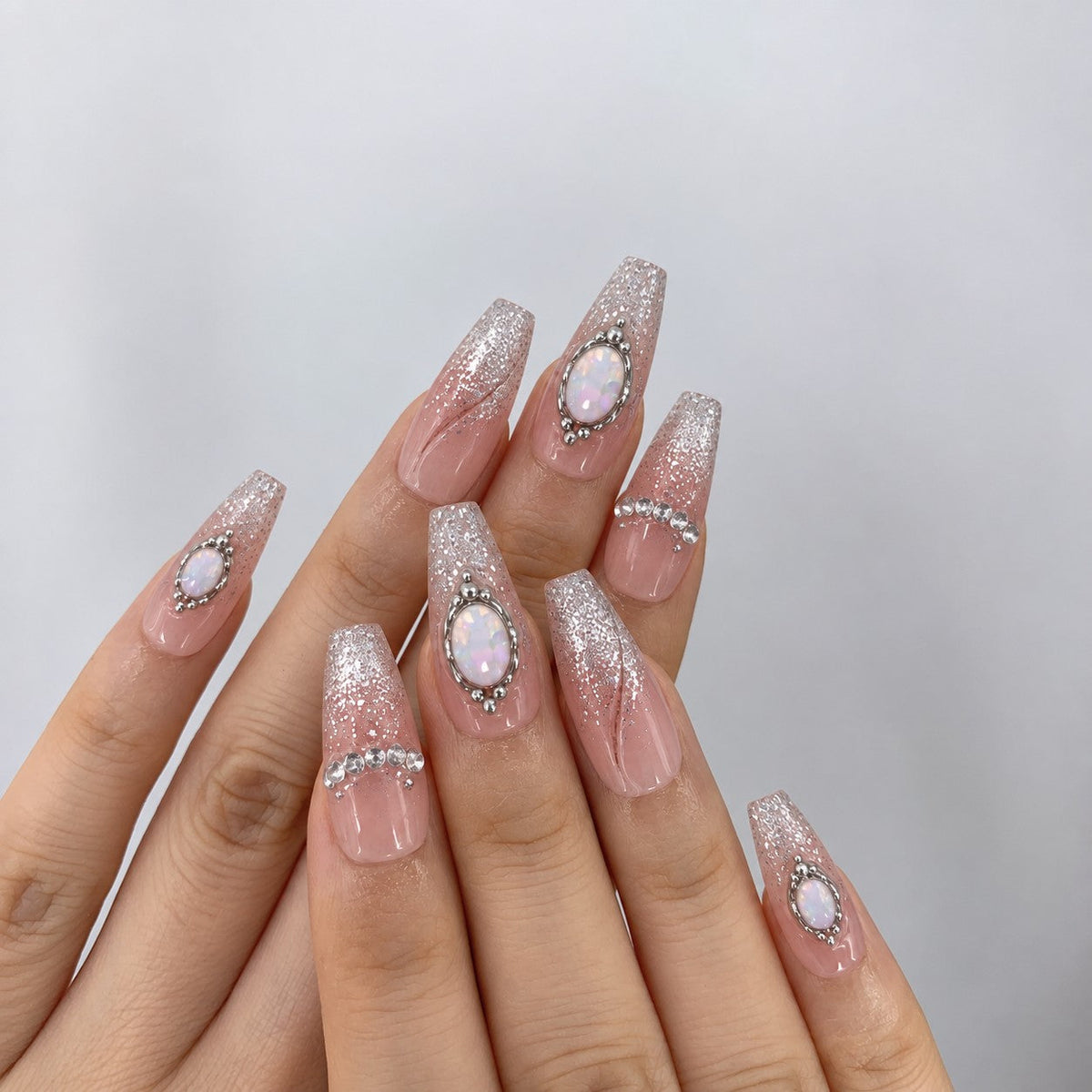 hand: Long coffin press-on nails in sheer pink nude with silver glitter and opal stones set in fine silver outlines.