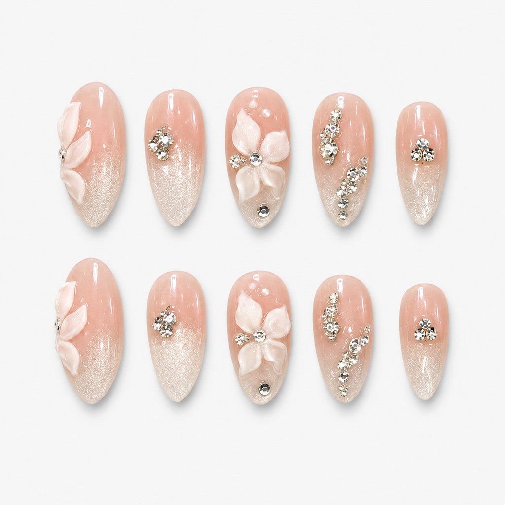 catalog: Almond medium press-on nails in milky nude with pearl shimmer, sculpted white 3D flowers and clear rhinestone accents.