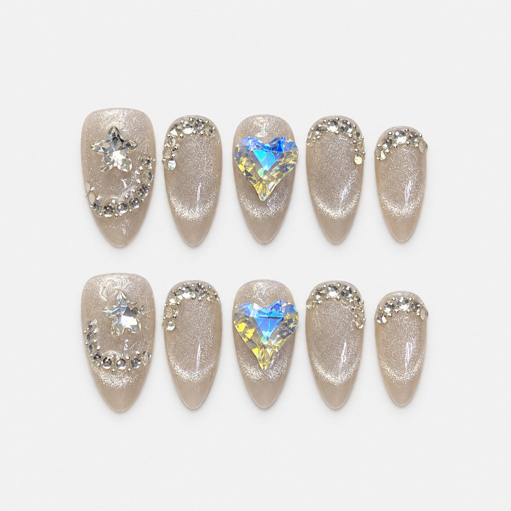 catalog: Medium almond press-on nails in icy greige cat-eye shimmer with clear crystal curves, a star gem and a large iridescent heart gem.