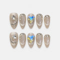 catalog: Medium almond press-on nails in icy greige cat-eye shimmer with clear crystal curves, a star gem and a large iridescent heart gem.