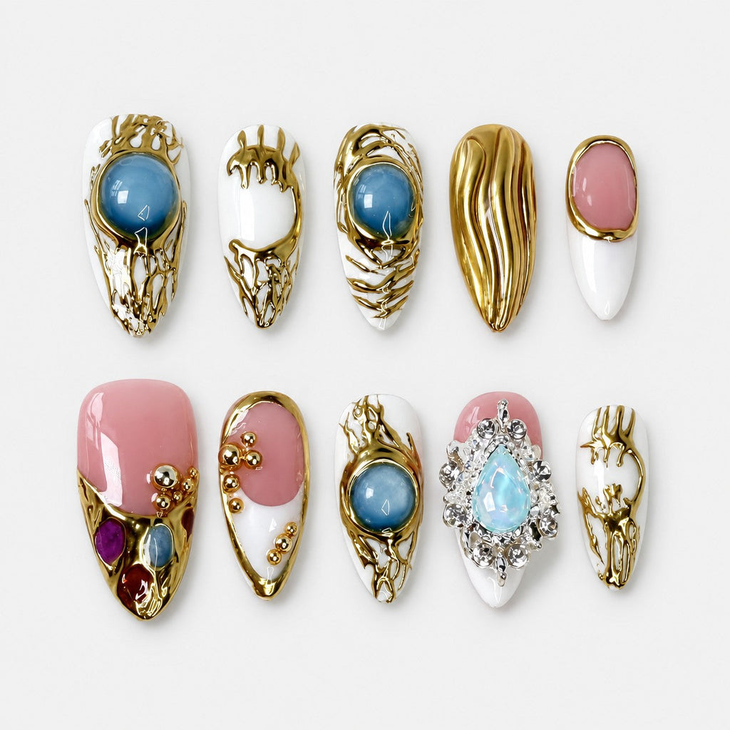 catalog: Medium almond press-on nails in white and pink with raised molten gold work, blue cabochon stones, gold beads and a crystal set opal charm.