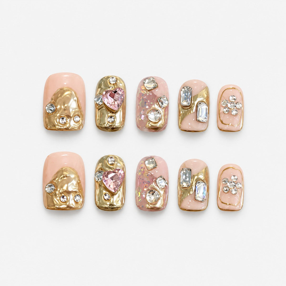catalog: Short square press-on nails in peach nude with sculpted gold foil shapes and clusters of clear and pink crystals.
