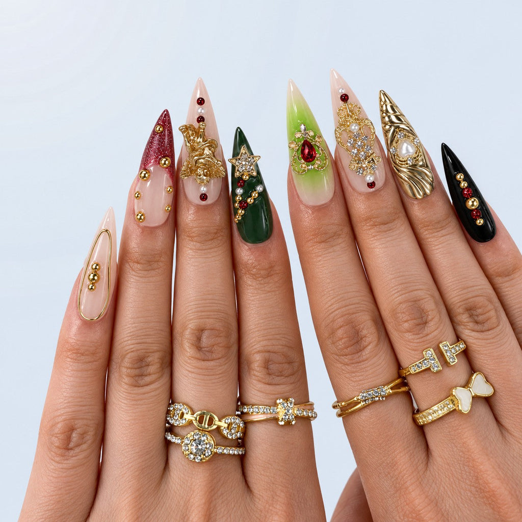 hand: Long stiletto press-on nails in green, oxblood, nude and black with gold cherub, cross and crown charms, pearls and red crystals.