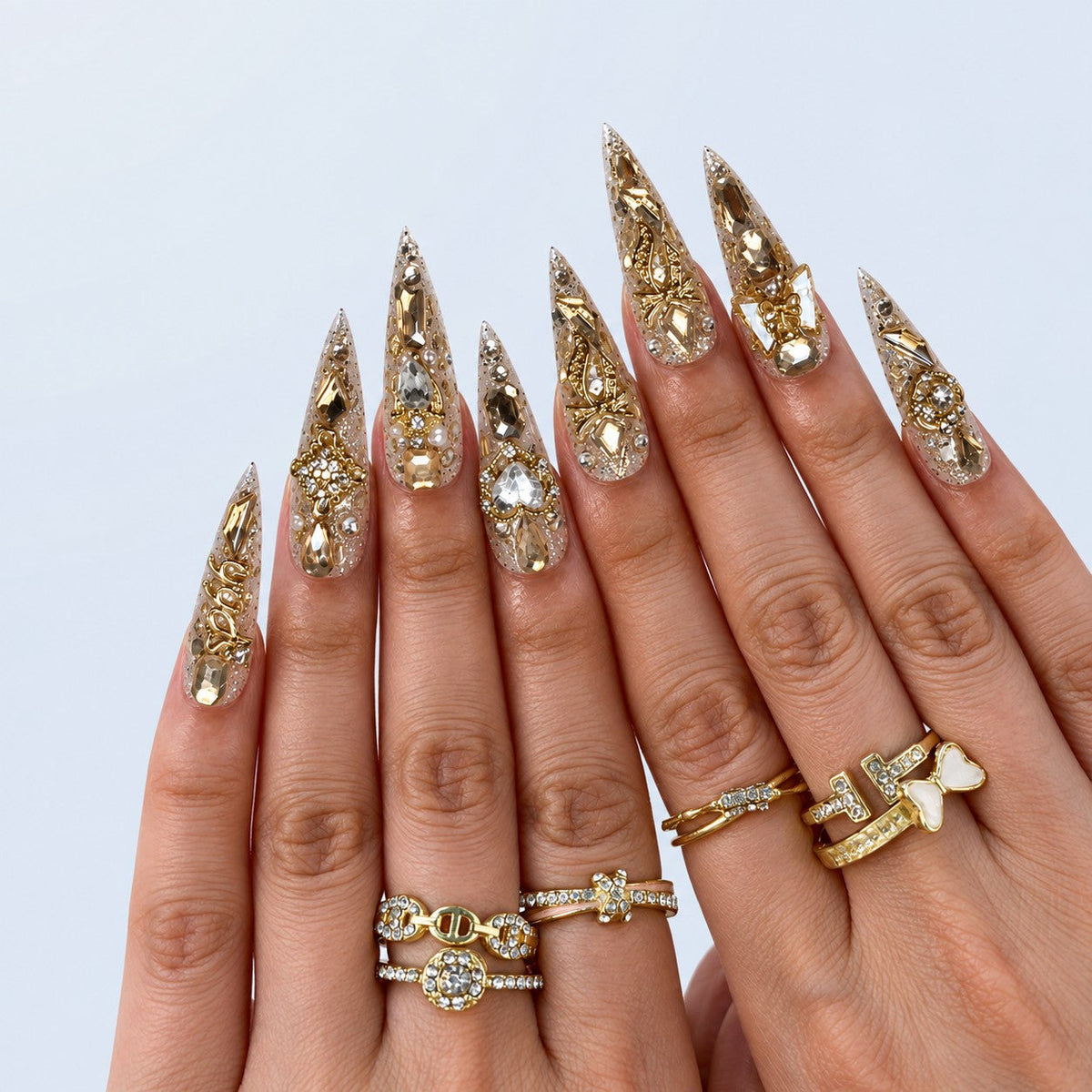 hand: Long stiletto press-on nails covered in champagne glitter with gold baroque scrollwork, clear rhinestones and mirrored gold shards.