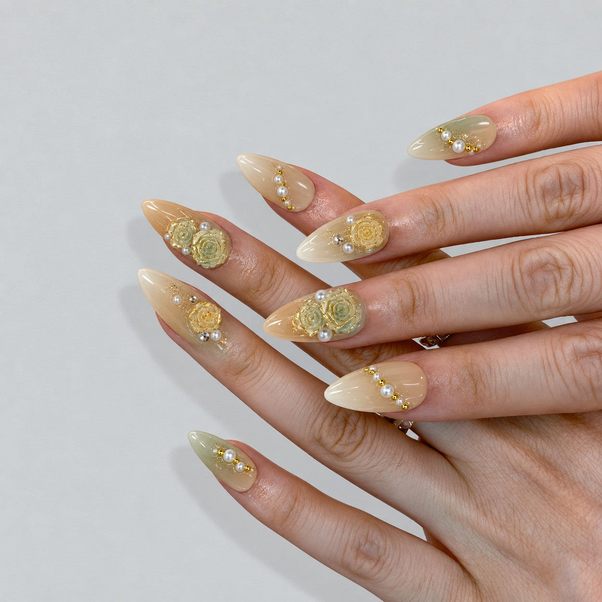 hand: Medium almond nails in cream and pale sage ombre with sculpted yellow and mint roses, gold leaf accents and strands of ivory pearls.