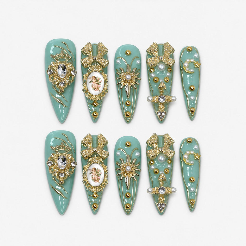 catalog: Long stiletto press-on nails in pale seafoam green with gold filigree, a cherub cameo, gold bows, clear stones and scattered pearls.