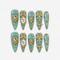 catalog: Long stiletto press-on nails in pale seafoam green with gold filigree, a cherub cameo, gold bows, clear stones and scattered pearls.
