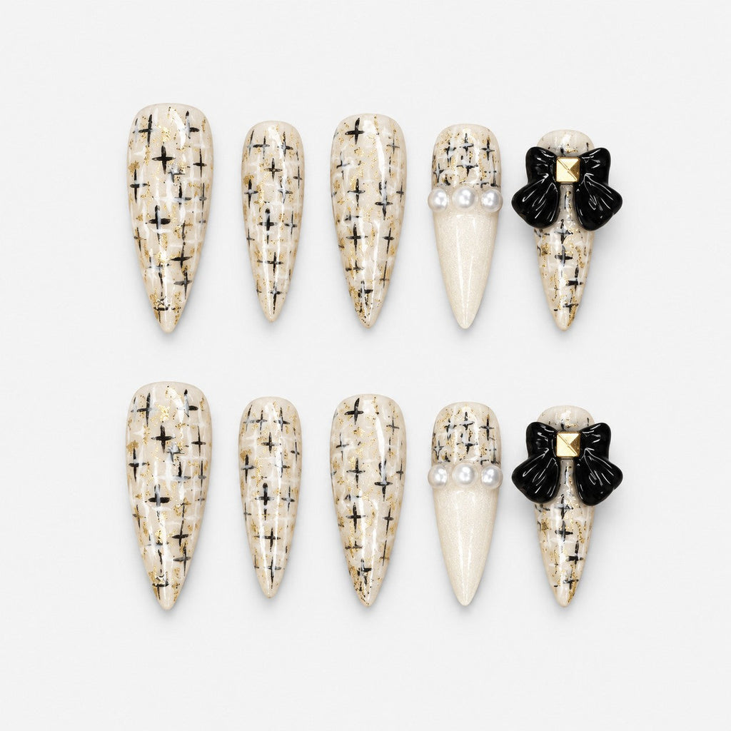 catalog: Long ivory stiletto nails with painted black and gold tweed, glossy black bows with gold studs and small pearls.