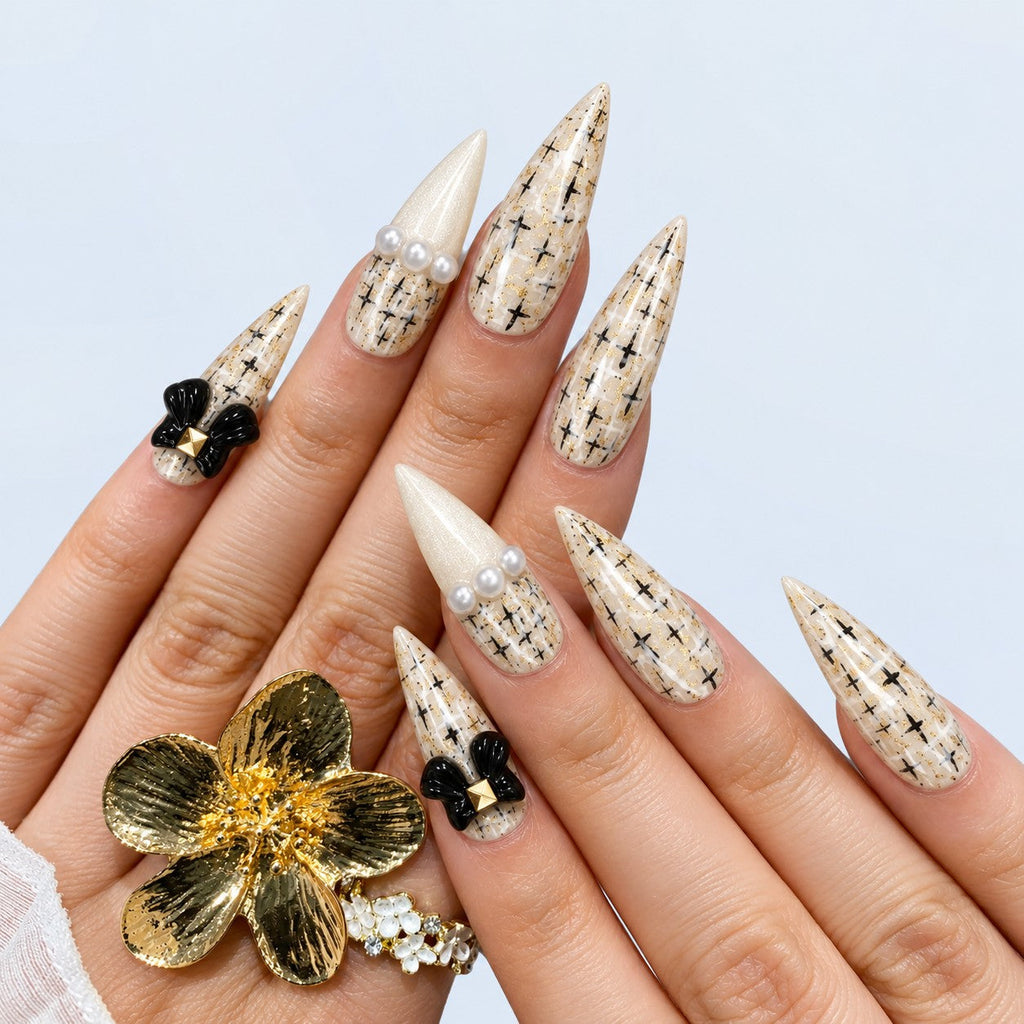 hand: Long ivory stiletto nails with painted black and gold tweed, glossy black bows with gold studs and small pearls.