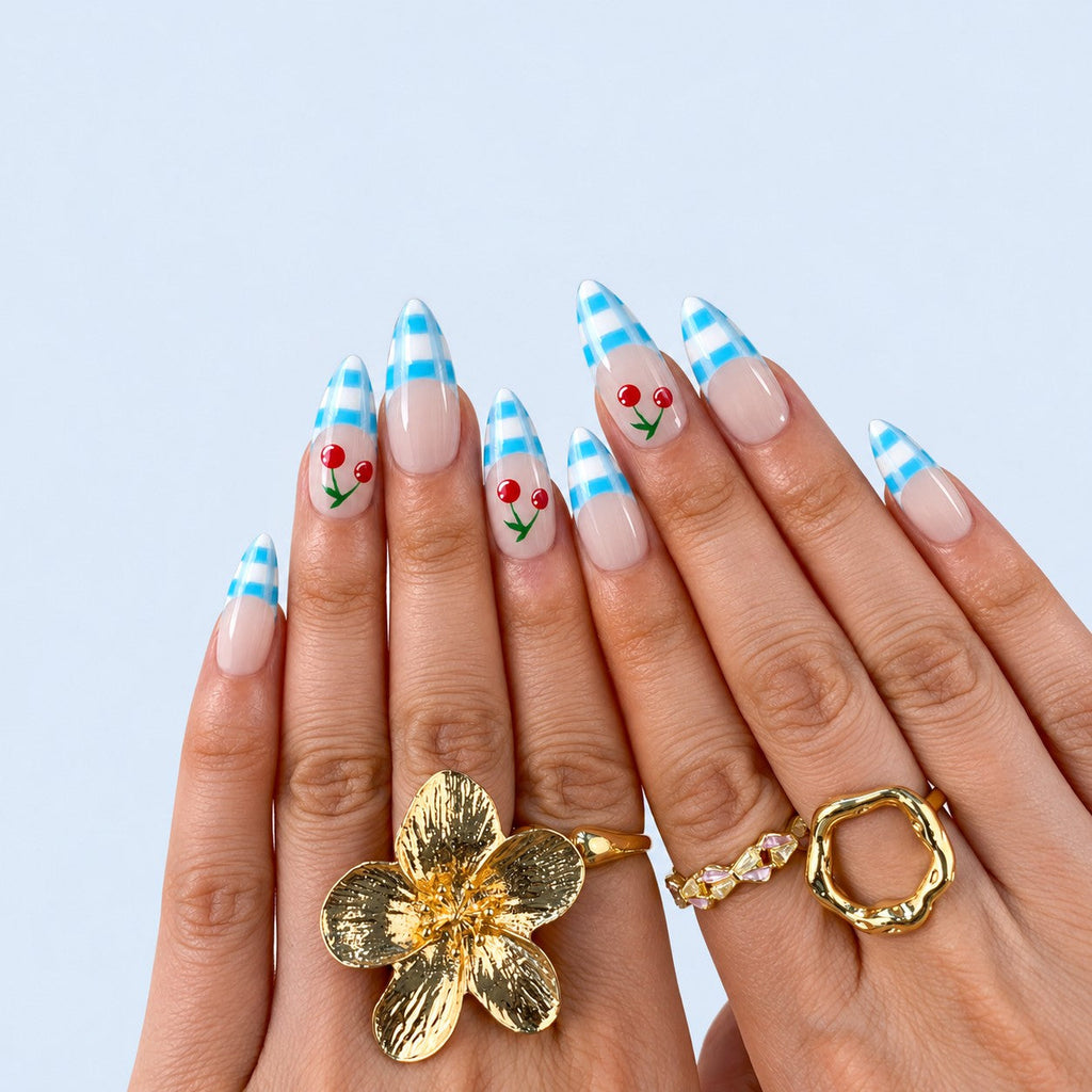 hand: Almond nails with nude base, blue and white gingham French tips and painted red cherries on two accent nails.
